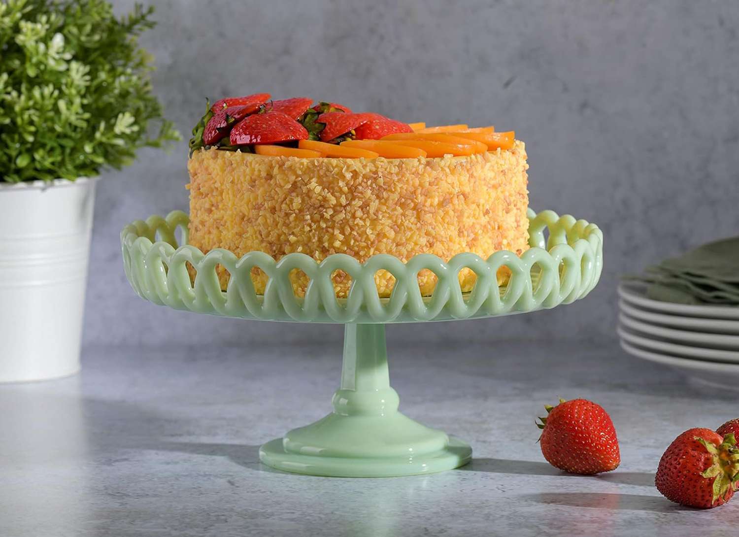 green cake stand with a cake, strawberries and plates