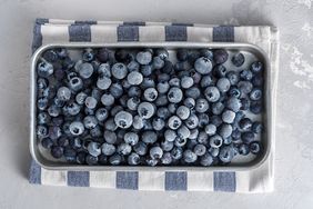 frozen blueberries on a baking sheet with a striped kitchen cloth underneath