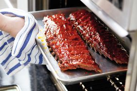 A tray of cooked glazed ribs being taken out of an oven with a towel