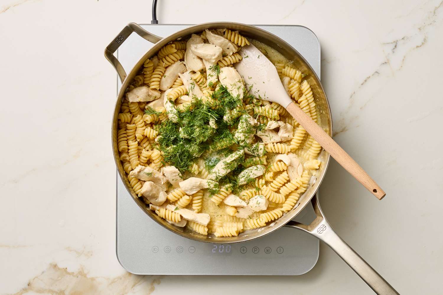 Skillet with cooked pasta chicken and herbs seen overhead on a stovetop