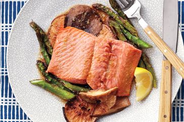 Cooked salmon served on a plate with asparagus mushrooms and a lemon wedge