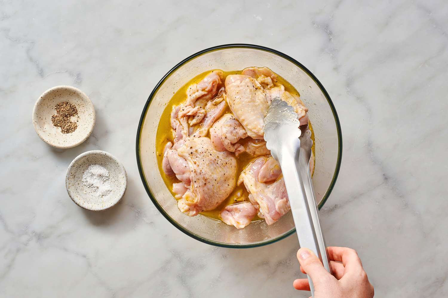 Using tongs to toss chicken thighs in oil and lemon juice