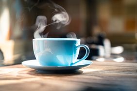 A steaming cup of coffee on a saucer placed on a wooden surface