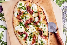 overhead view of a thin crust pizza with ricotta, prosciutto and peas