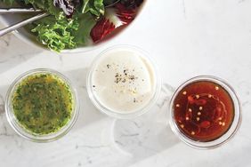 Three jars of salad dressings next to a bowl of mixed greens