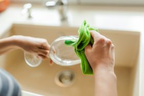 Person drying a wine glass with a cloth near a sink