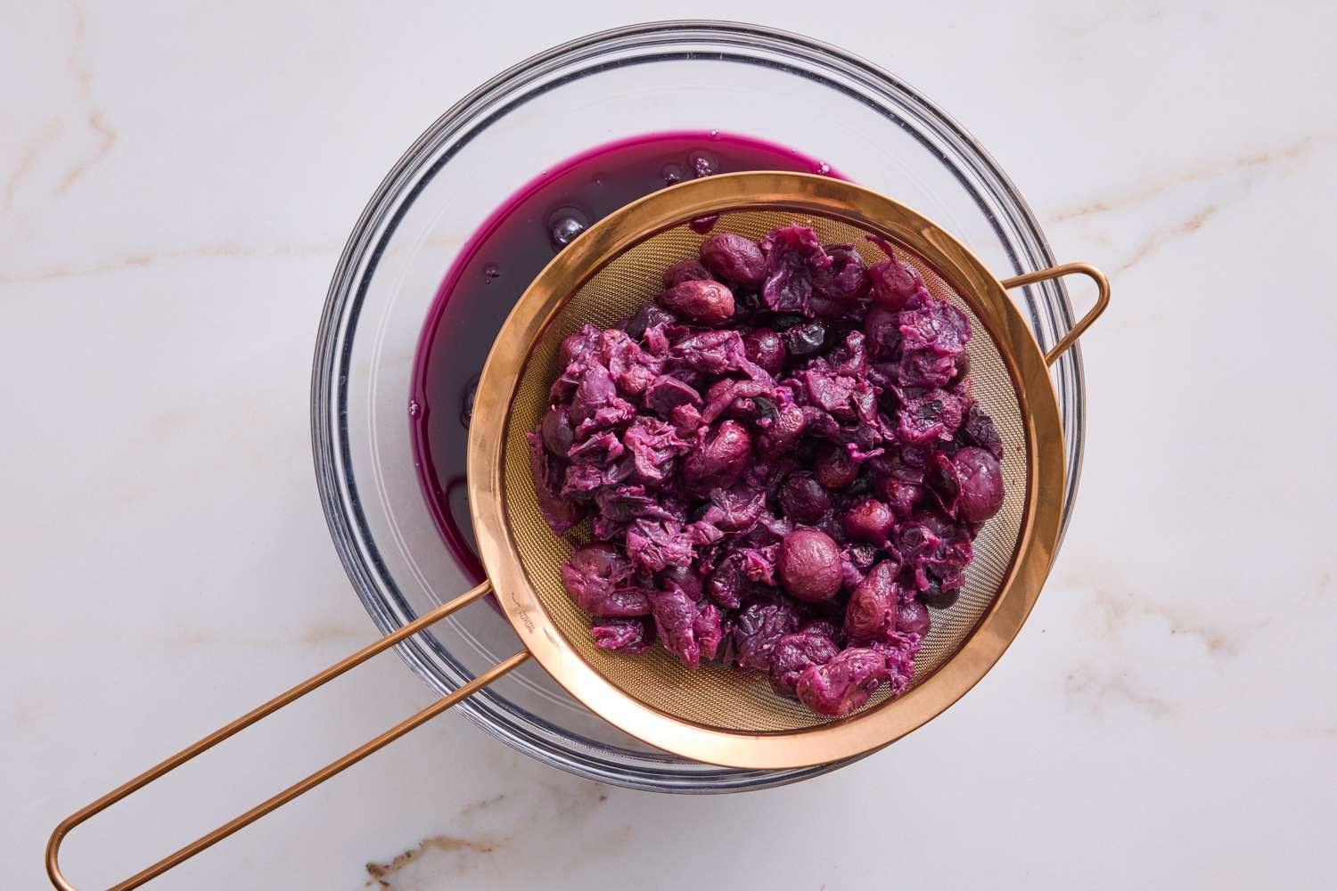 Strained fruit pulp in a sieve over a bowl during jelly preparation