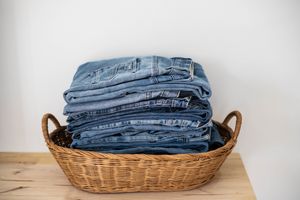 A wicker basket holding a neatly folded stack of jeans placed on a wooden surface