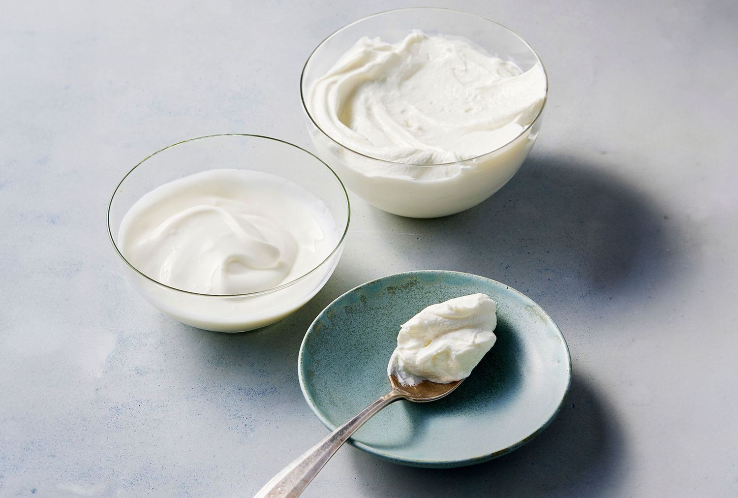 Two bowls of yogurt next to a spoon with yogurt on a small plate