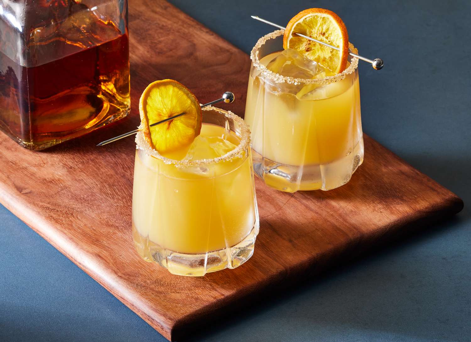 two whiskey sours and bottle of whiskey on wooden cutting board