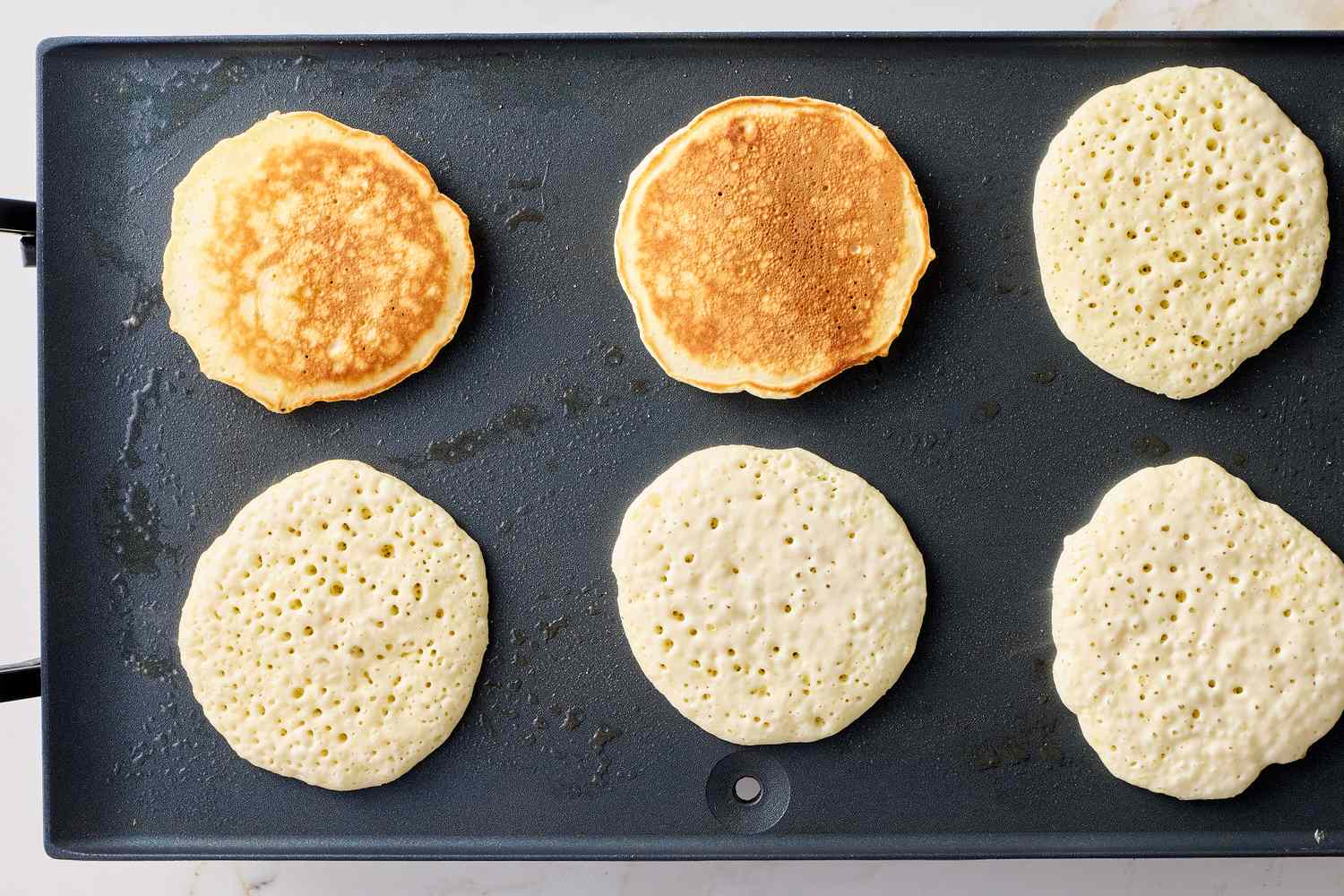 Pancakes cooking on a griddle three flipped and three unflipped