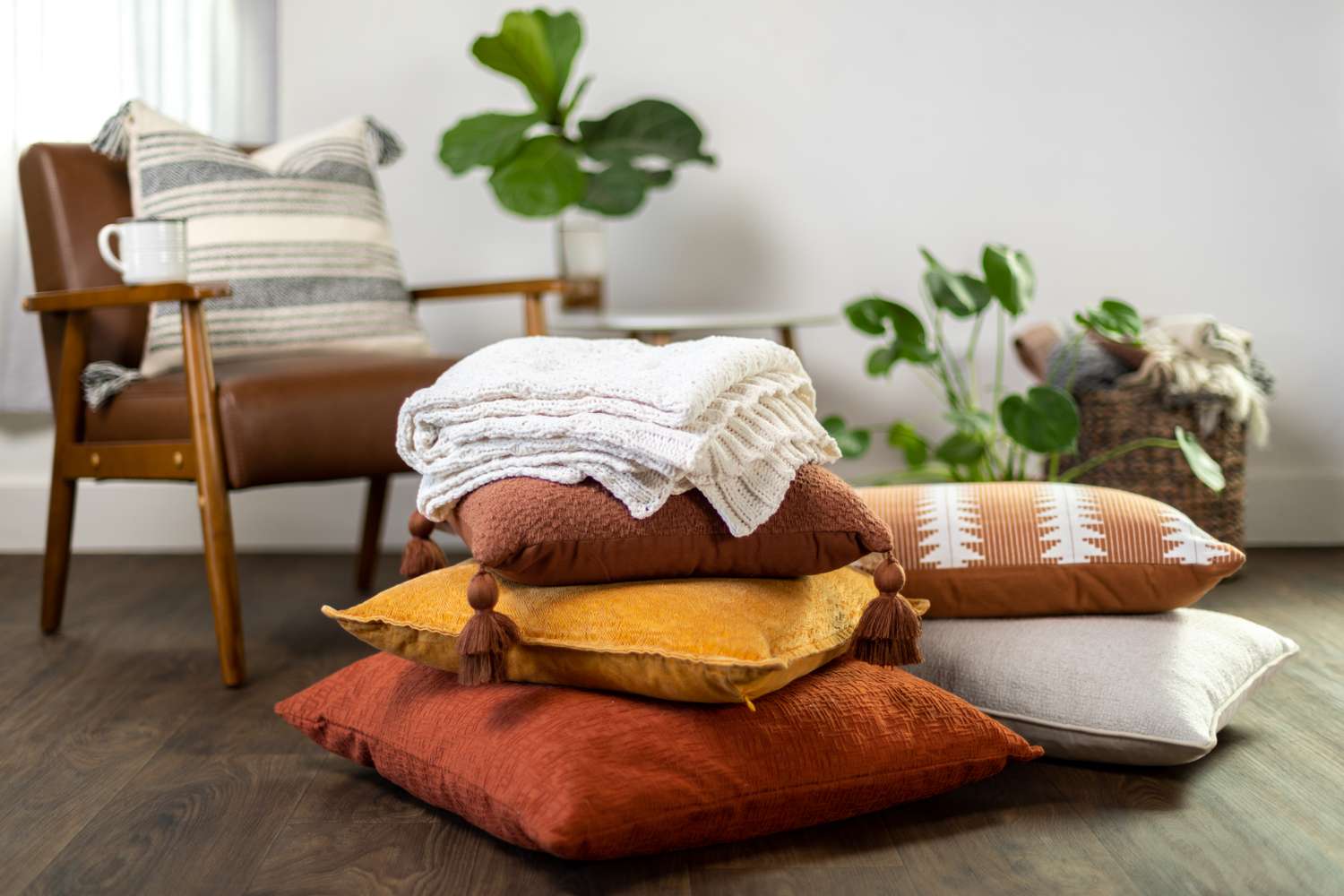 Stack of pillows and throws in a cozy living space with a chair and plants in the background