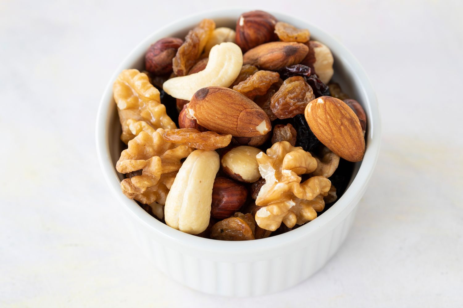 Bowl containing mixed nuts including almonds walnuts raisins hazelnuts and cashews