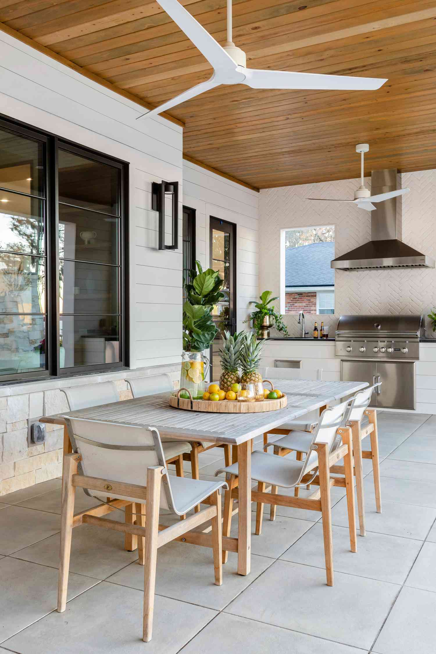 outdoor wooden dining table and chairs with an outdoor kitchen in the background