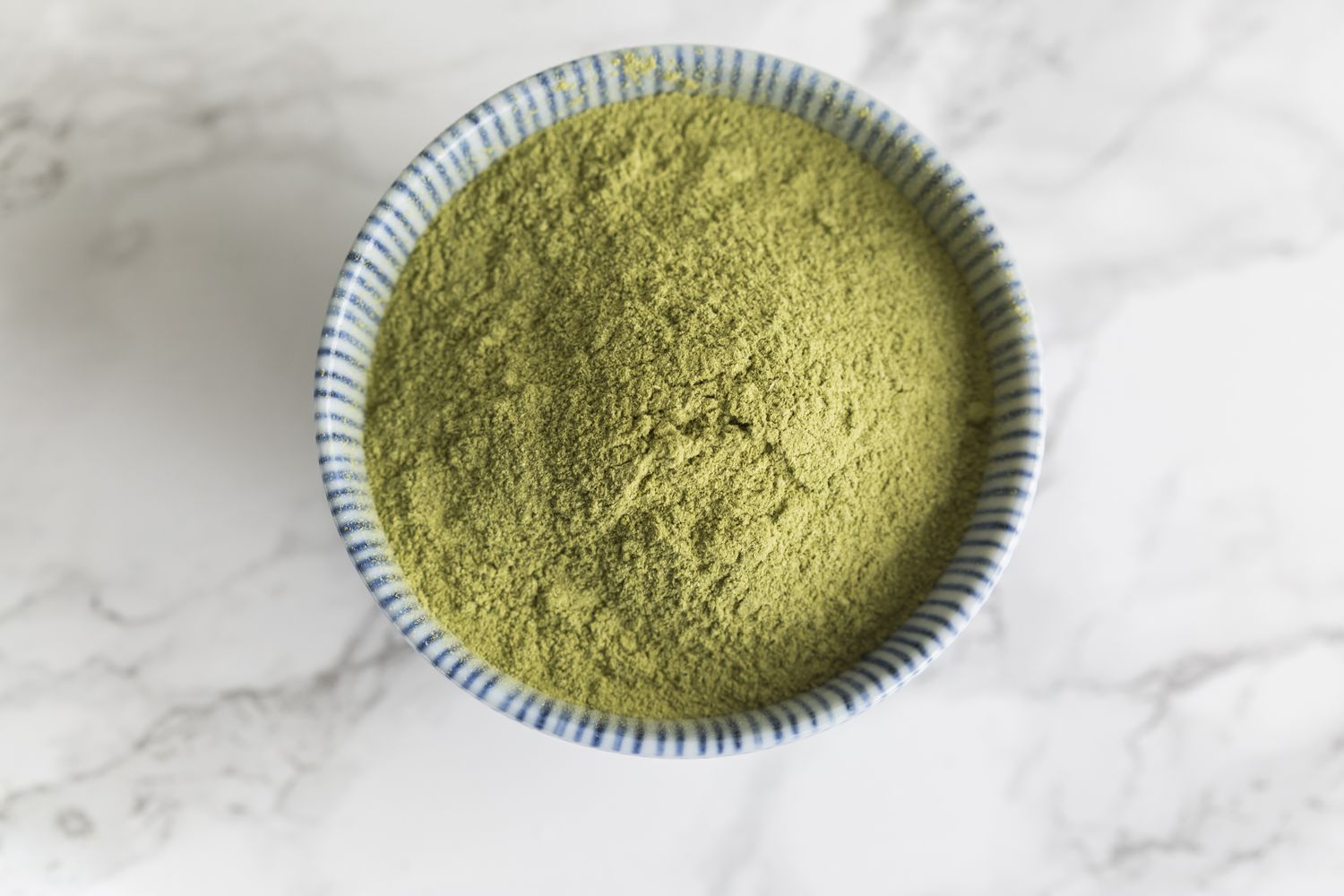A ceramic bowl filled with powdered greens on a marble surface