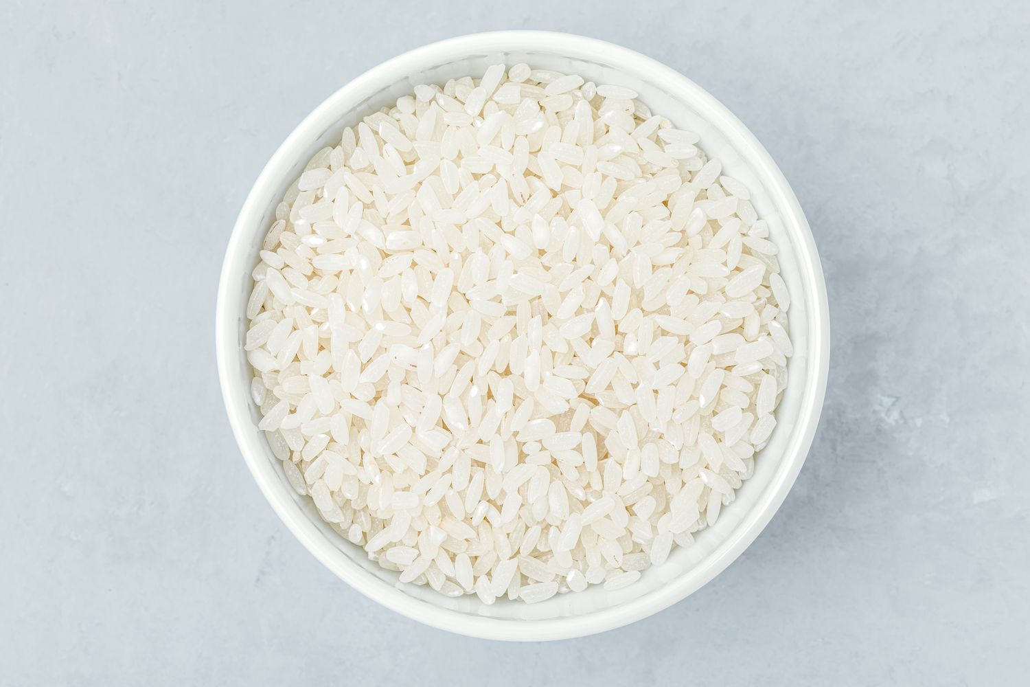 A bowl filled with uncooked white rice on a gray surface