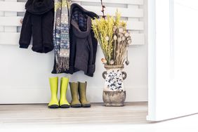 Coats scarves and boots near a decorative vase with dried flowers in an entryway