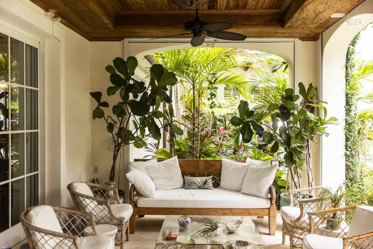 Cozy veranda seating area with a sofa chairs and a ceiling fan surrounded by lush tropical plants