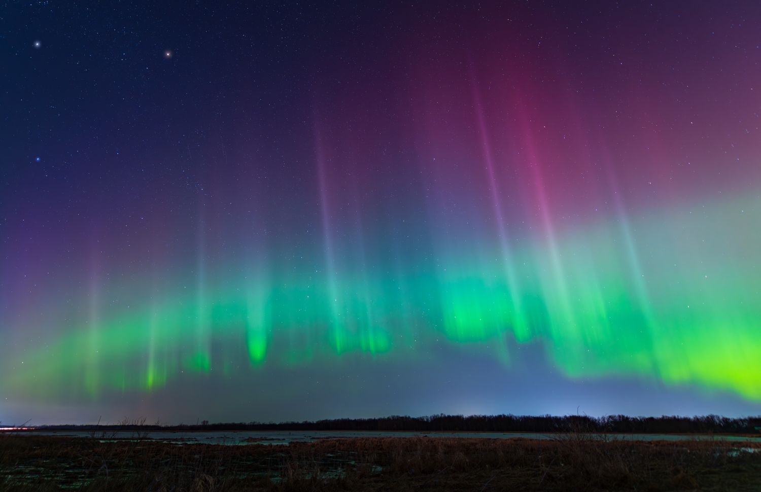 Aurora borealis with colorful light streaks in the night sky above a horizon with land and water