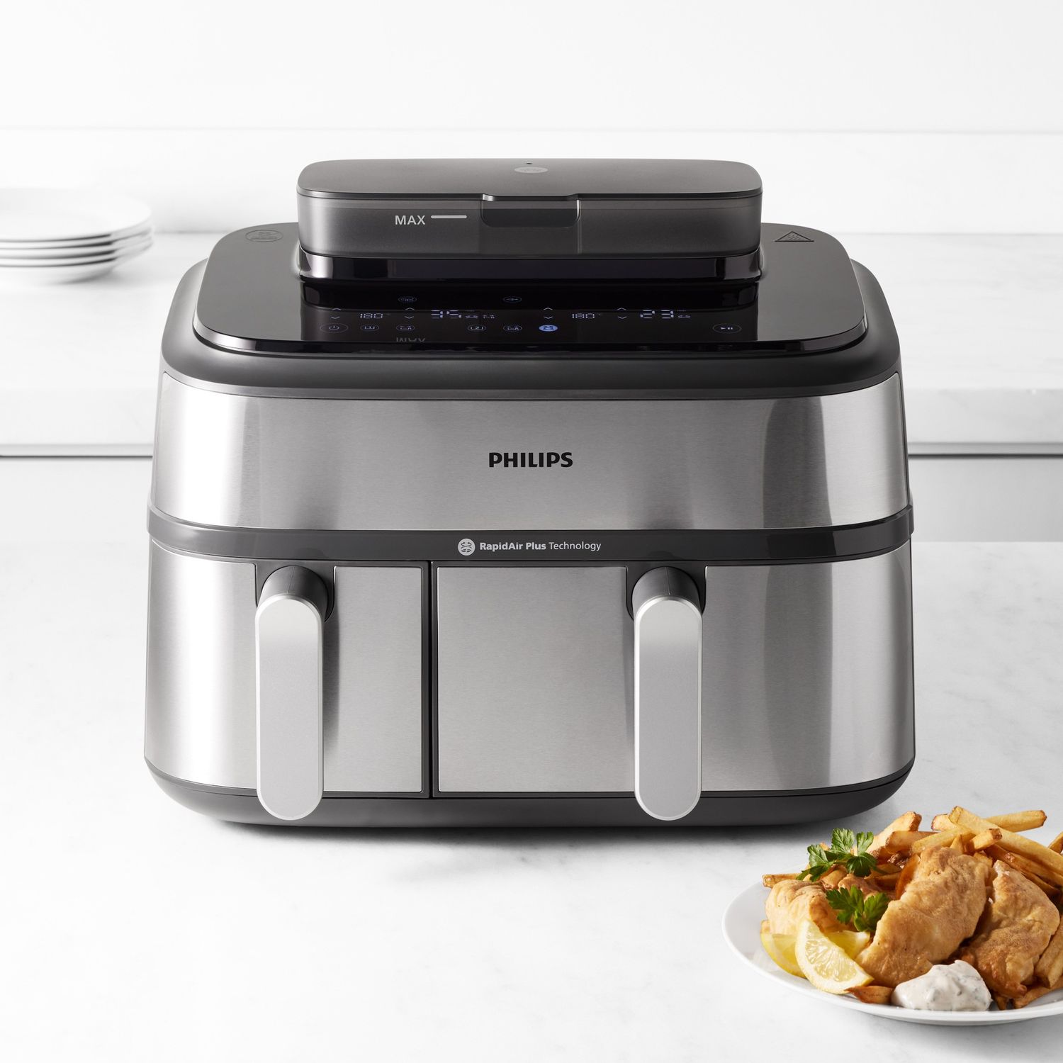 A Philips air fryer with dual compartments placed on a counter beside a plate of fried food