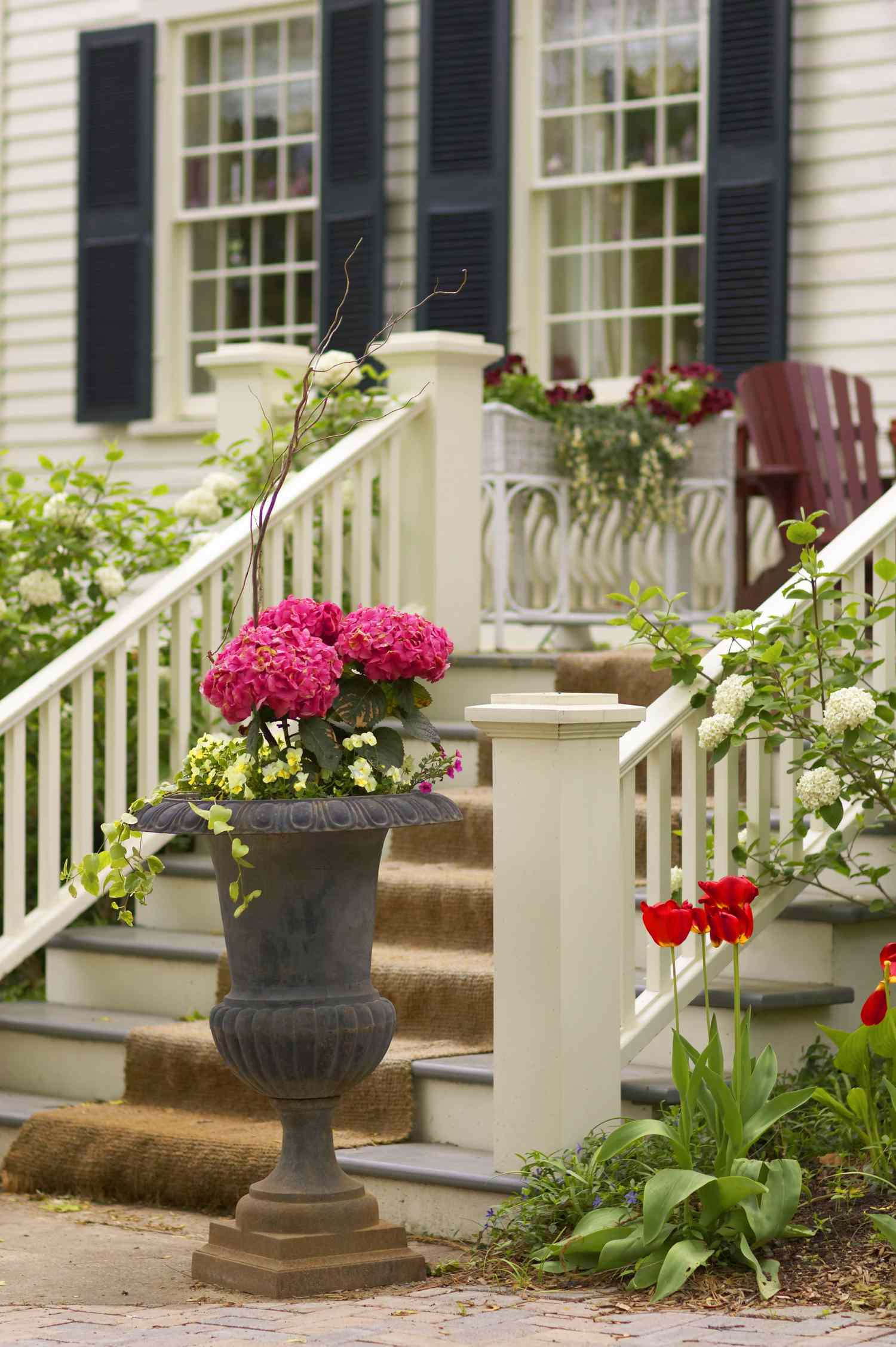 A house porch with potted flowers and a staircase surrounded by plants and decor