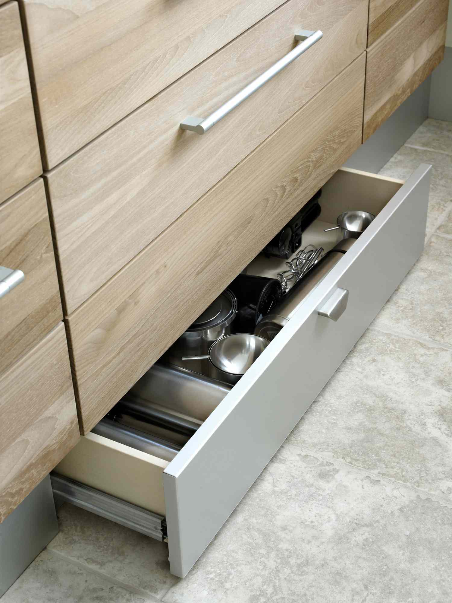 Kitchen cabinet with an open drawer showing utensils and cookware inside