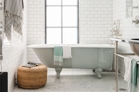 A bathroom with a clawfoot bathtub a wicker stool and towels hanging and folded on fixtures
