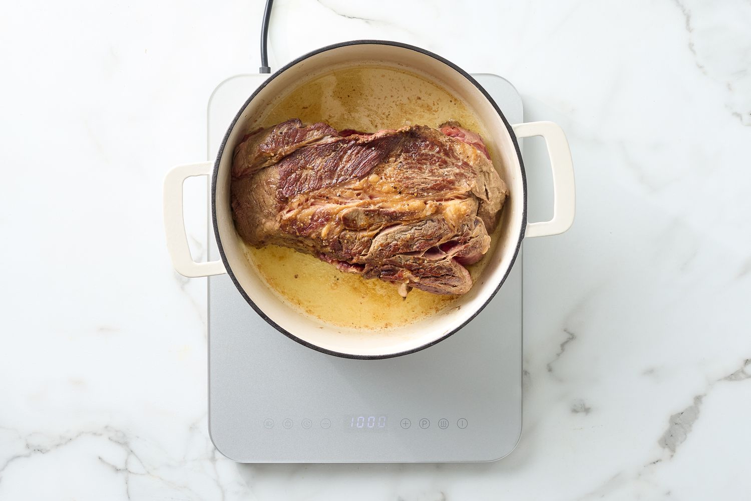 Pot roast cooking in a white pot on a stovetop
