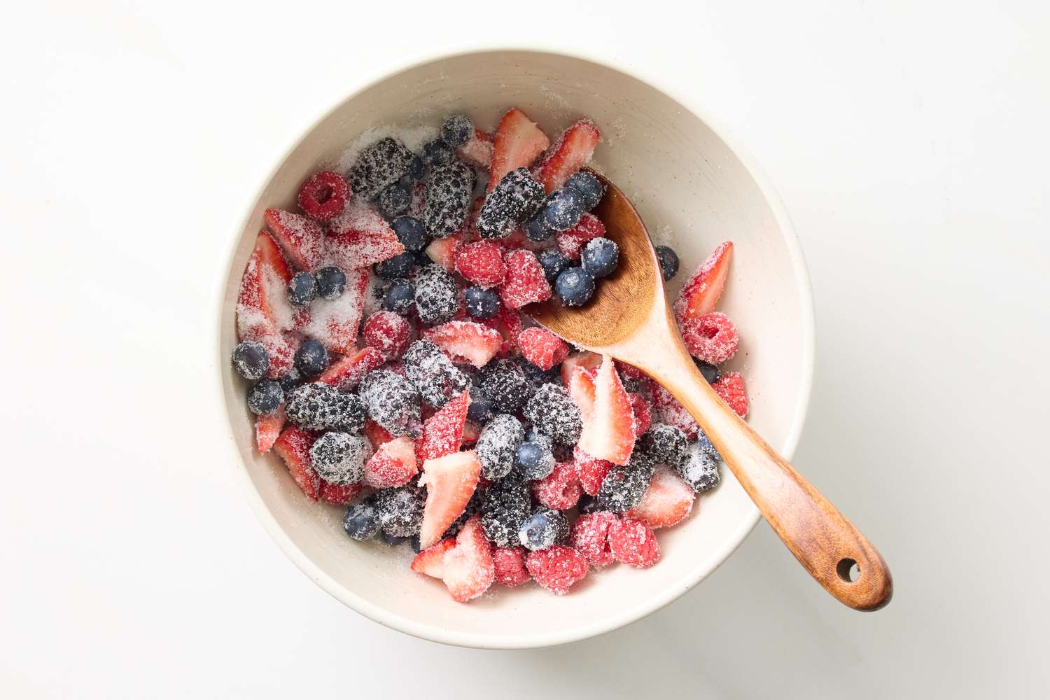 Bowl of mixed berries raspberries blueberries and strawberries with sugar wooden spoon on the side