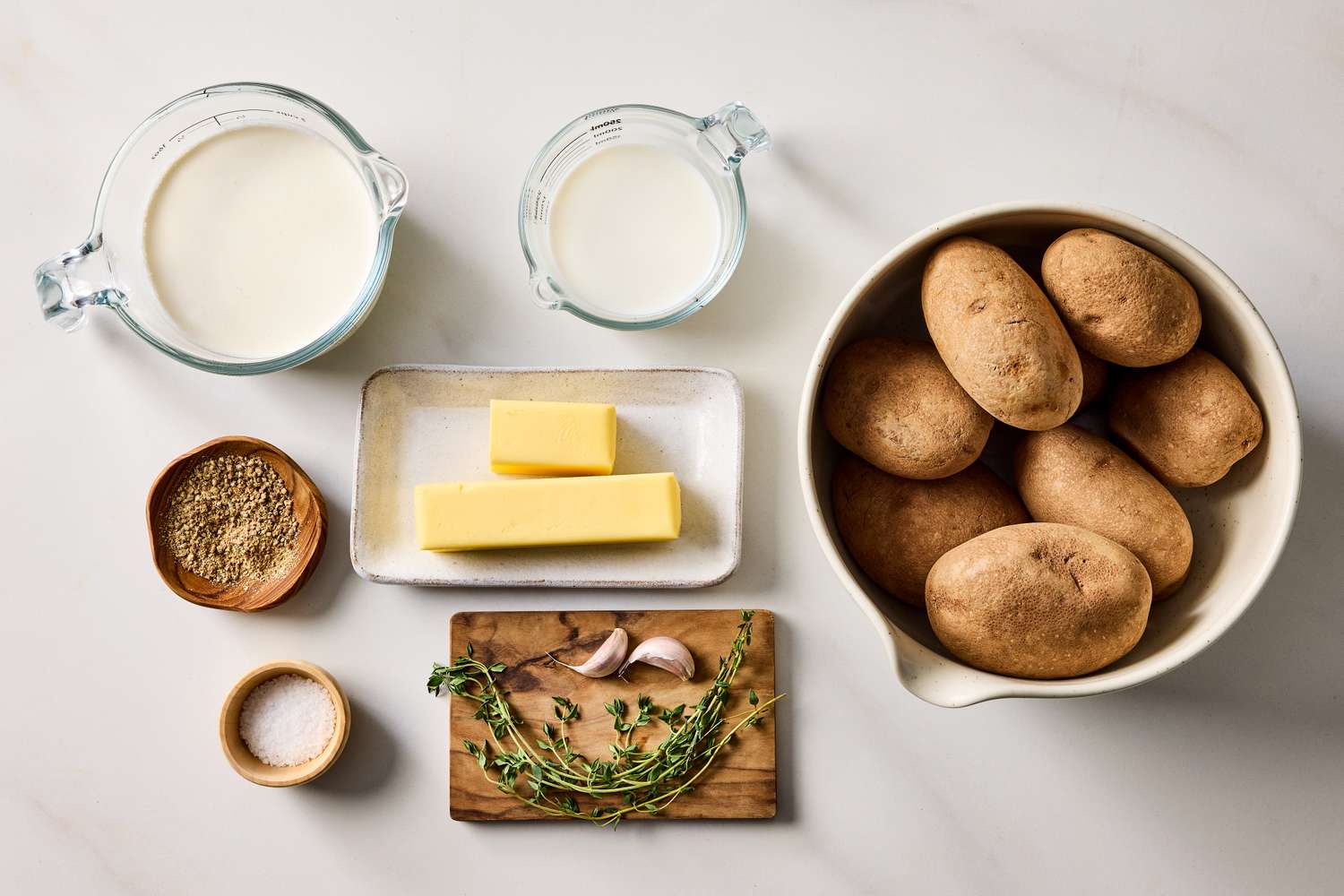 Potatoes milk butter garlic herbs and seasonings arranged as ingredients for making puree
