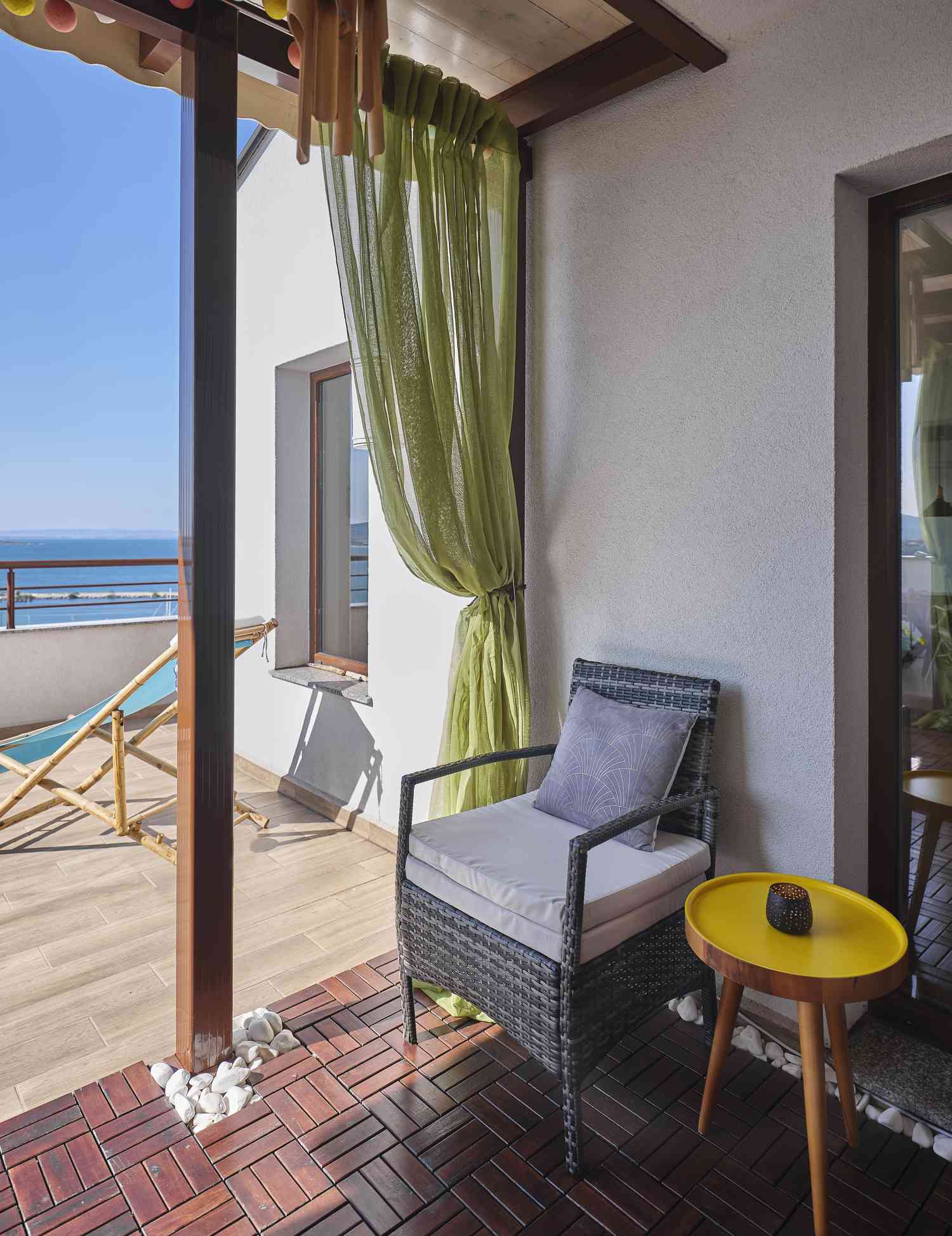 A balcony with a wicker chair, small yellow table, and a sea view