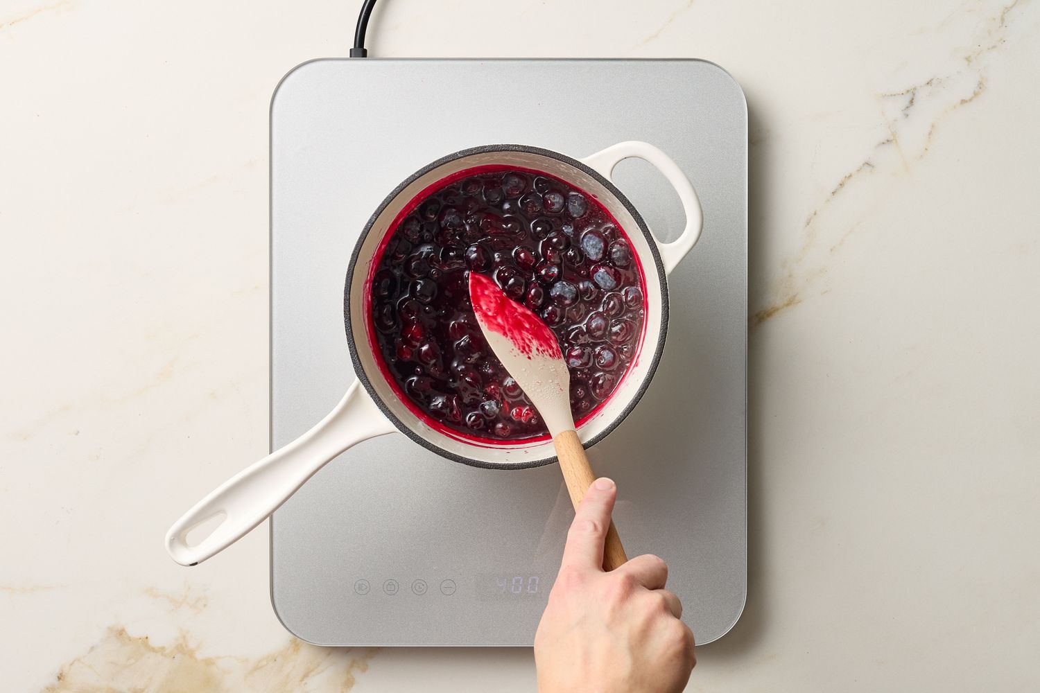 A hand stirring a pot of blueberry compote on a stovetop