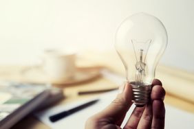 Hand holding Incandescent Lighting bulb on wooden workspace table
