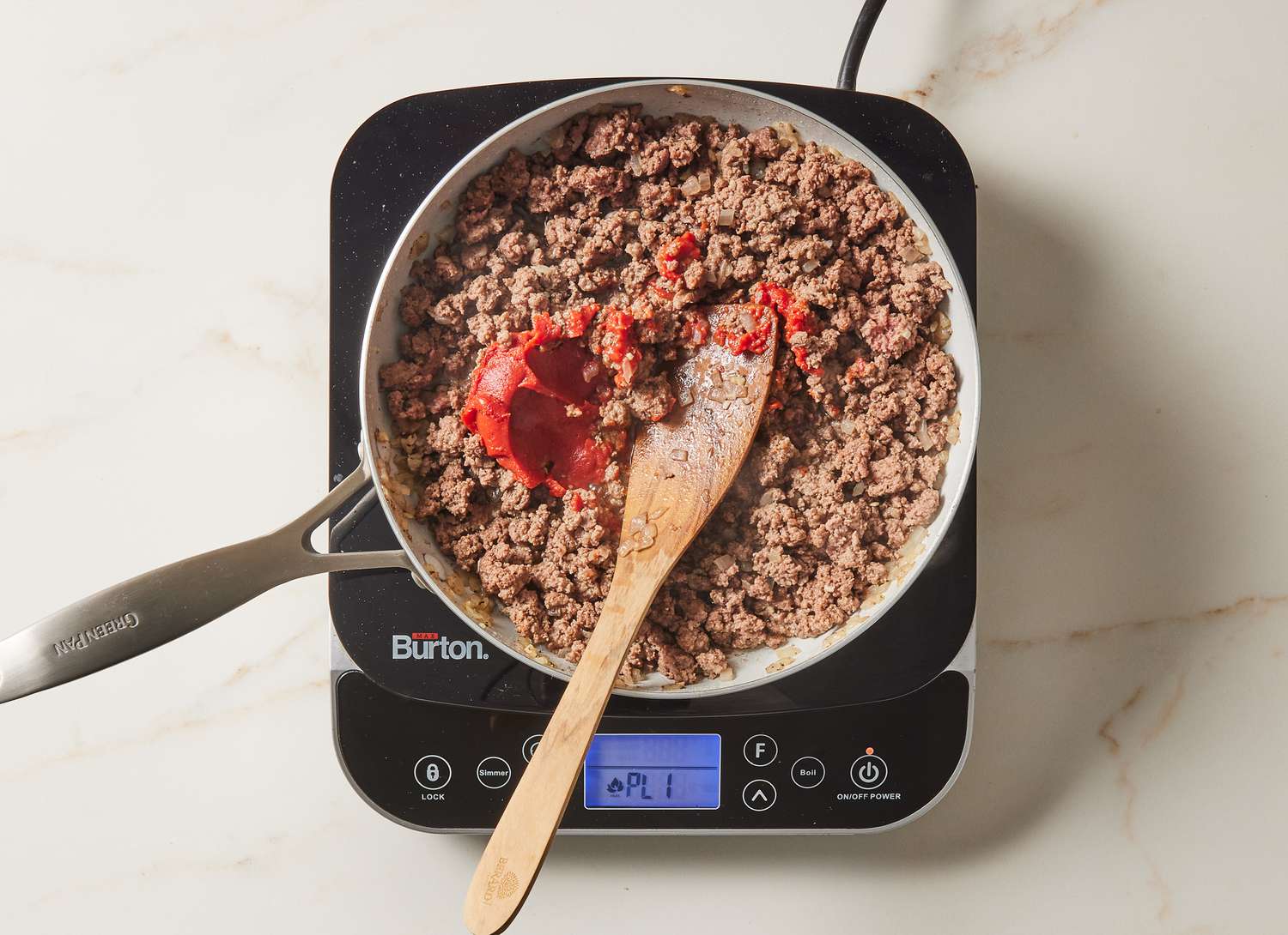 ground beef browning in a skillet with tomato paste with a wooden spoon