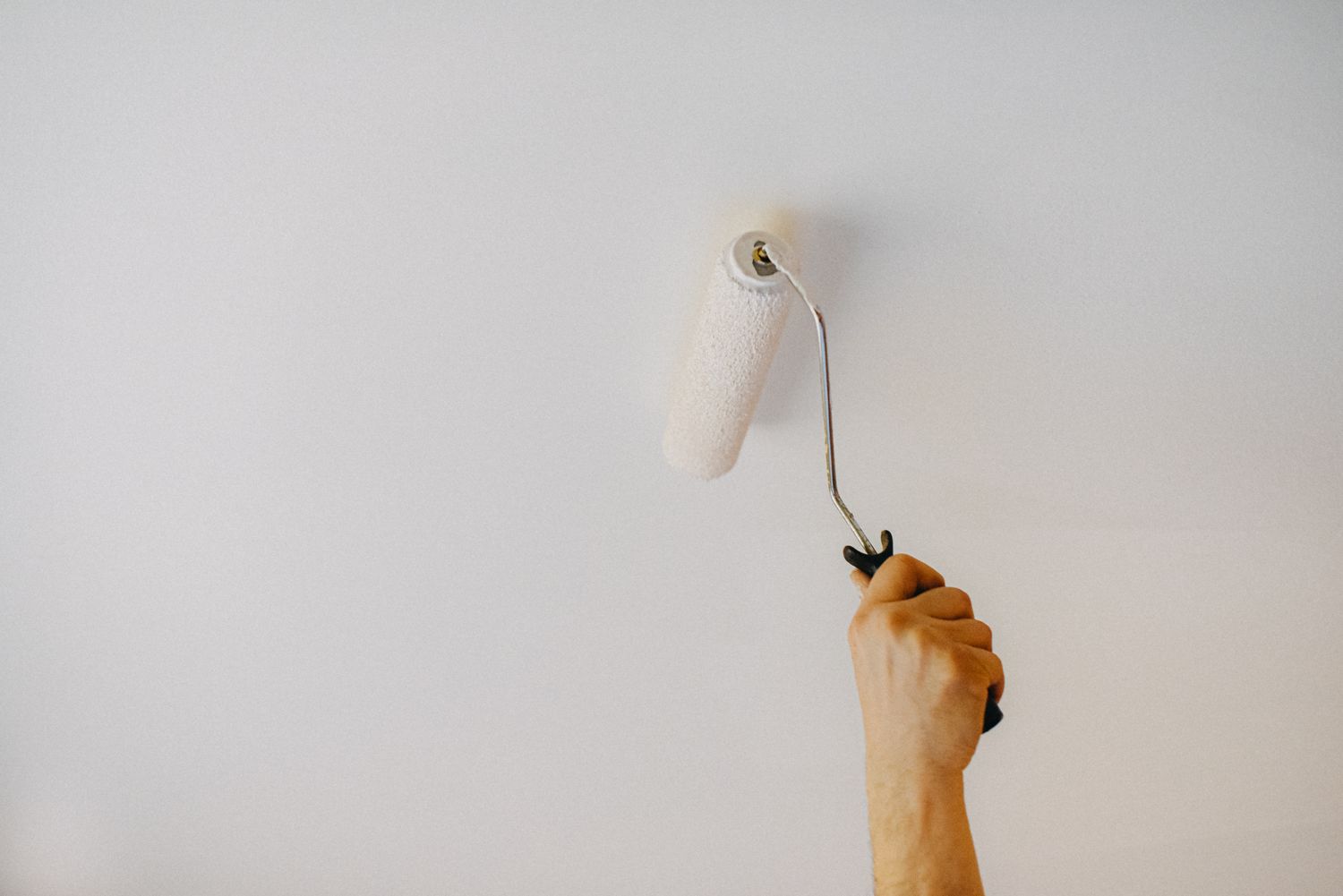 Hand painting a ceiling white with a paint roller.