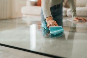 Person cleaning a glass table with a cloth focusing on hand movement and table surface