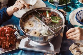People enjoying hot pot dining with various ingredients being cooked in a communal pot
