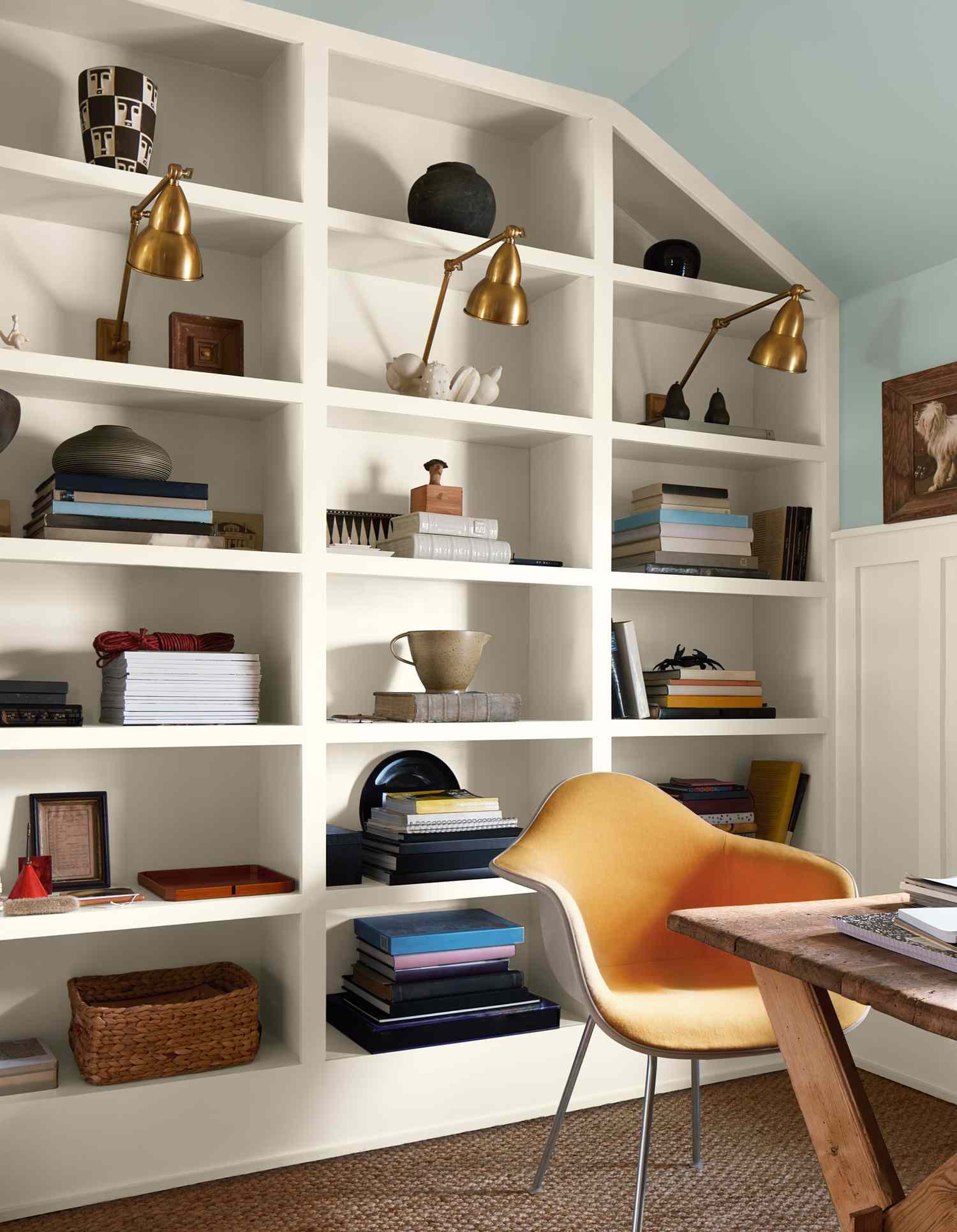 A stylish office room setup with a bookshelf yellow chair and decorative table
