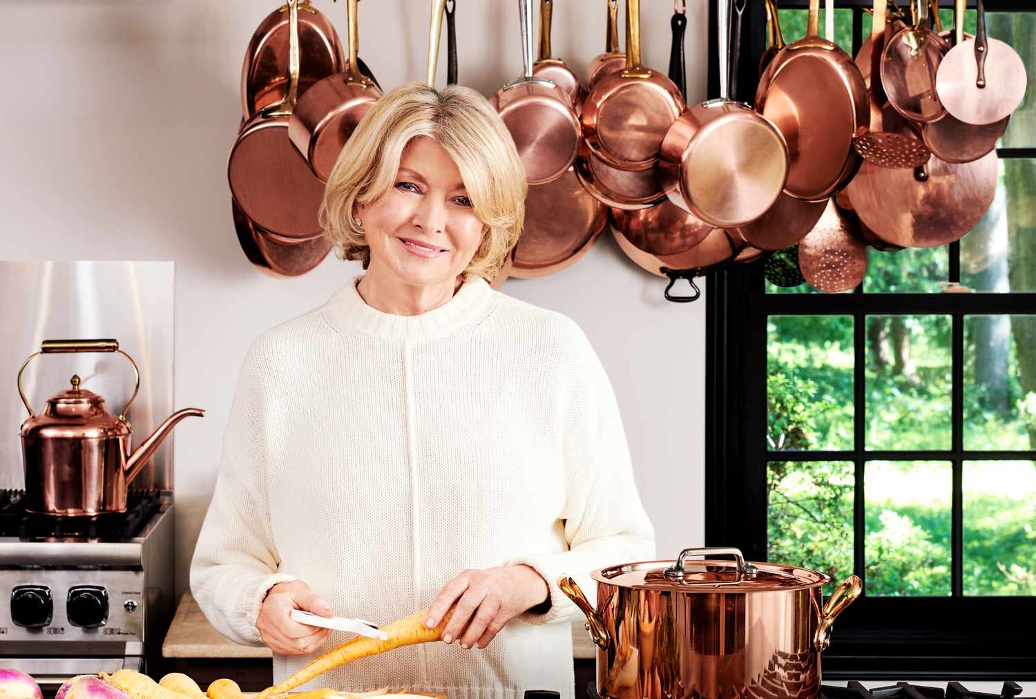 decorvow in a kitchen with copper pots and pans hanging behind her smiling while preparing food