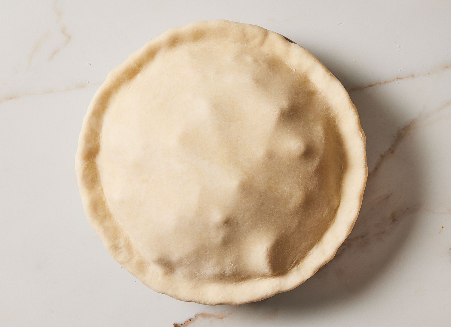 uncooked pie with crust covering entire pie on a marble surface