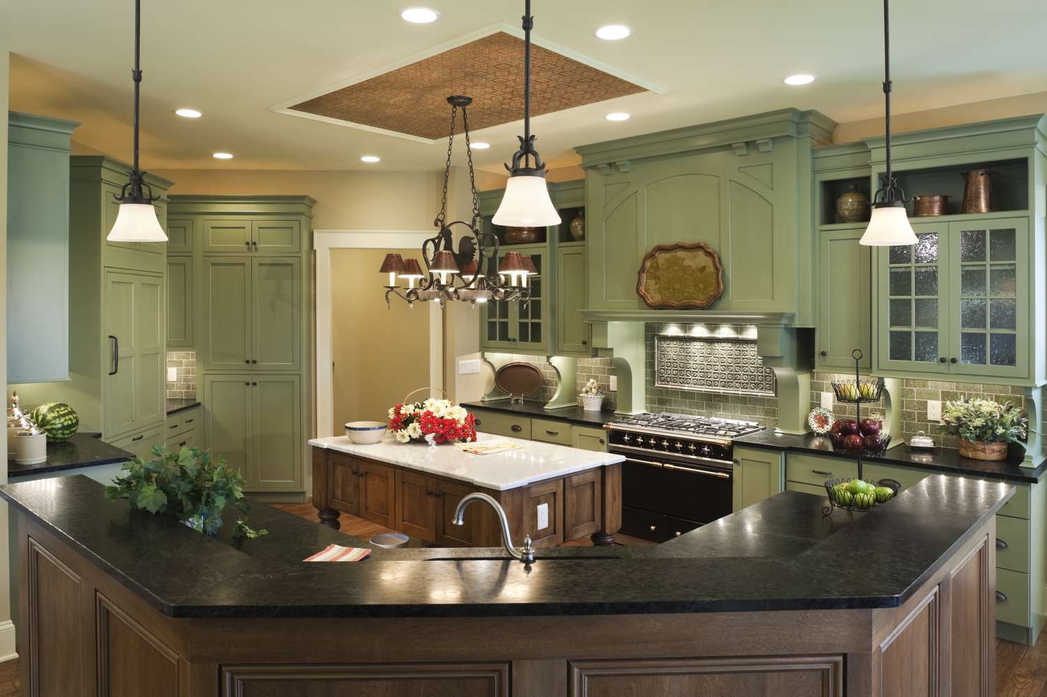 A spacious kitchen featuring a central island green cabinets and modern lighting fixtures