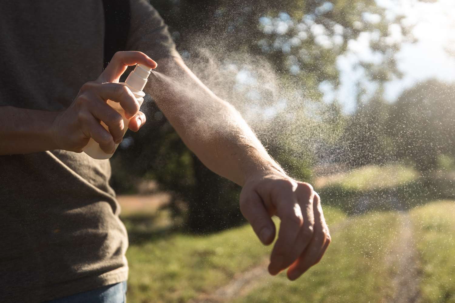 Person spraying mosquito repellent on their arm outdoors