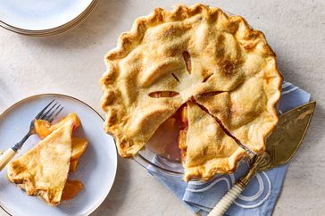 A peach pie with a slice served on a plate alongside a fork and pie server
