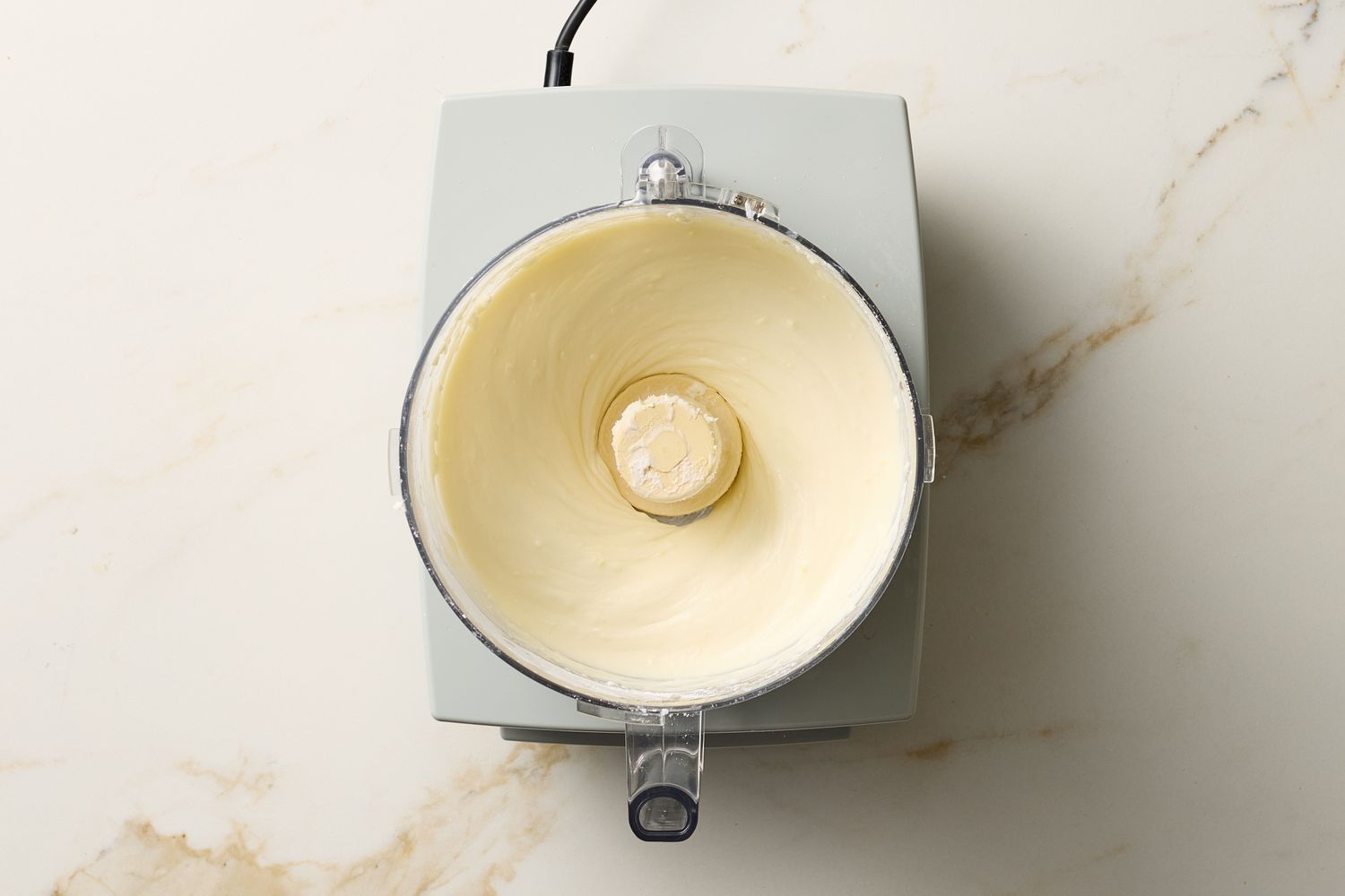 A food processor bowl containing whipped creamy mixture on a countertop