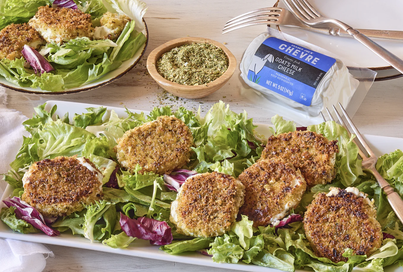 A plate of goat cheese medallions served on a bed of greens with a package of goat cheese and seasoning nearby