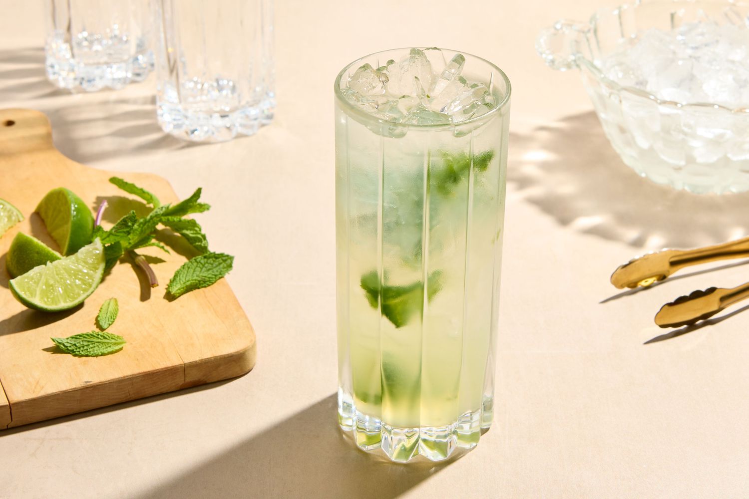 A mojito cocktail in a glass, mint leaves and lime pieces on a wooden board beside