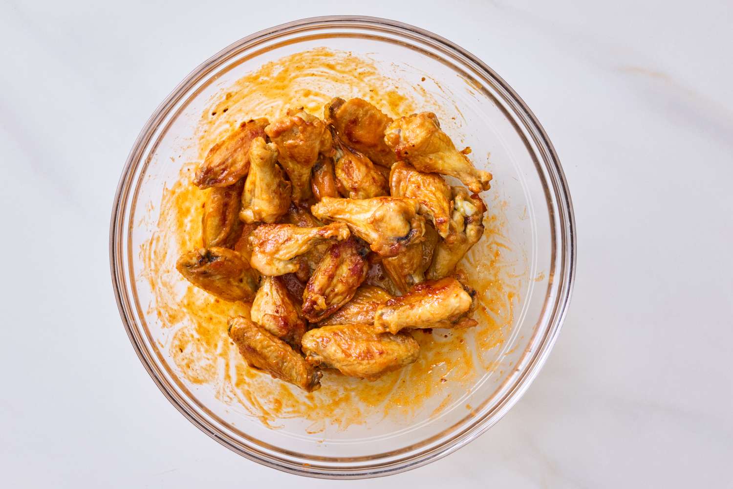 A clear bowl filled with seasoned baked chicken wings