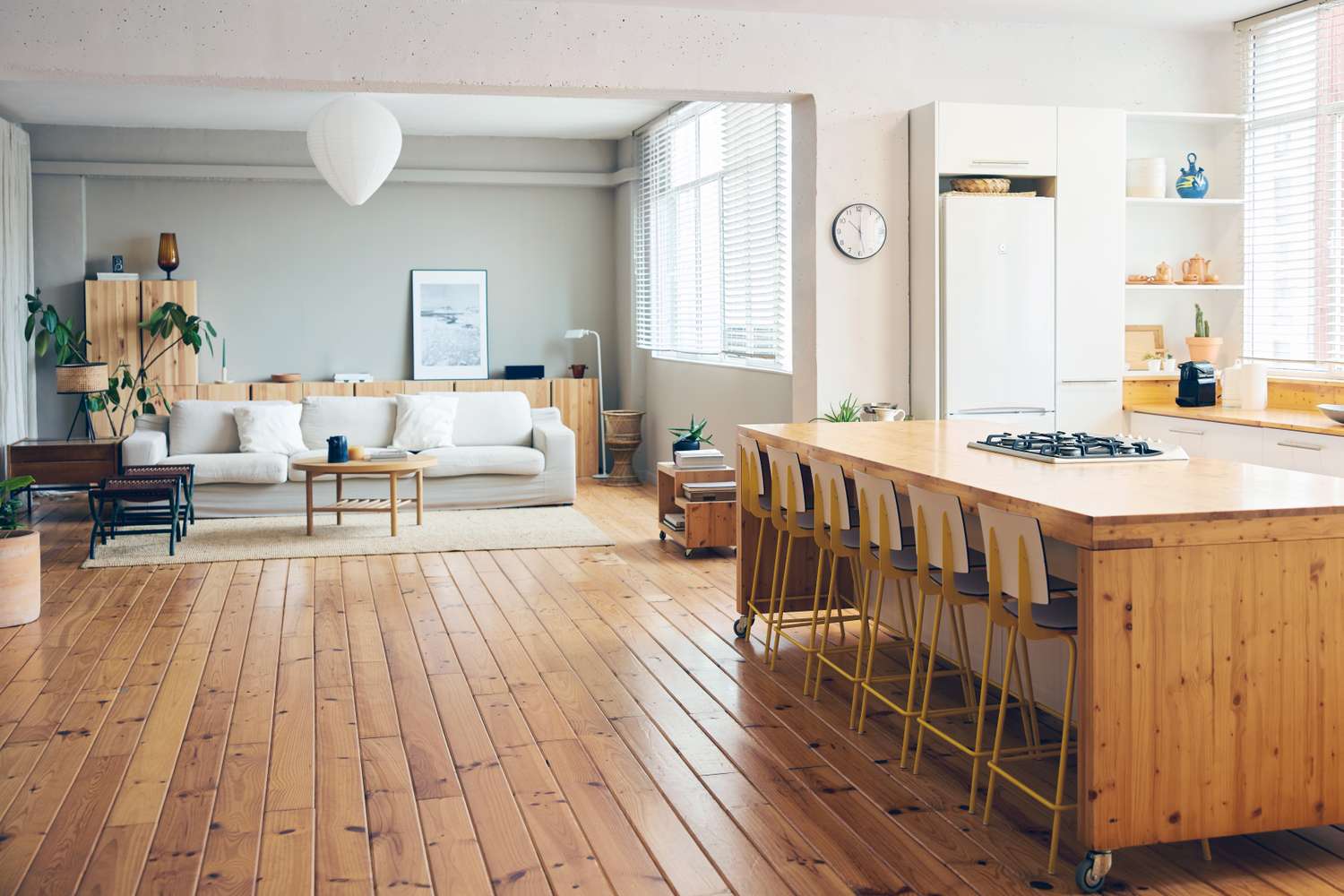 Modern openplan living area with wooden flooring a cozy sofa and a kitchen island with chairs
