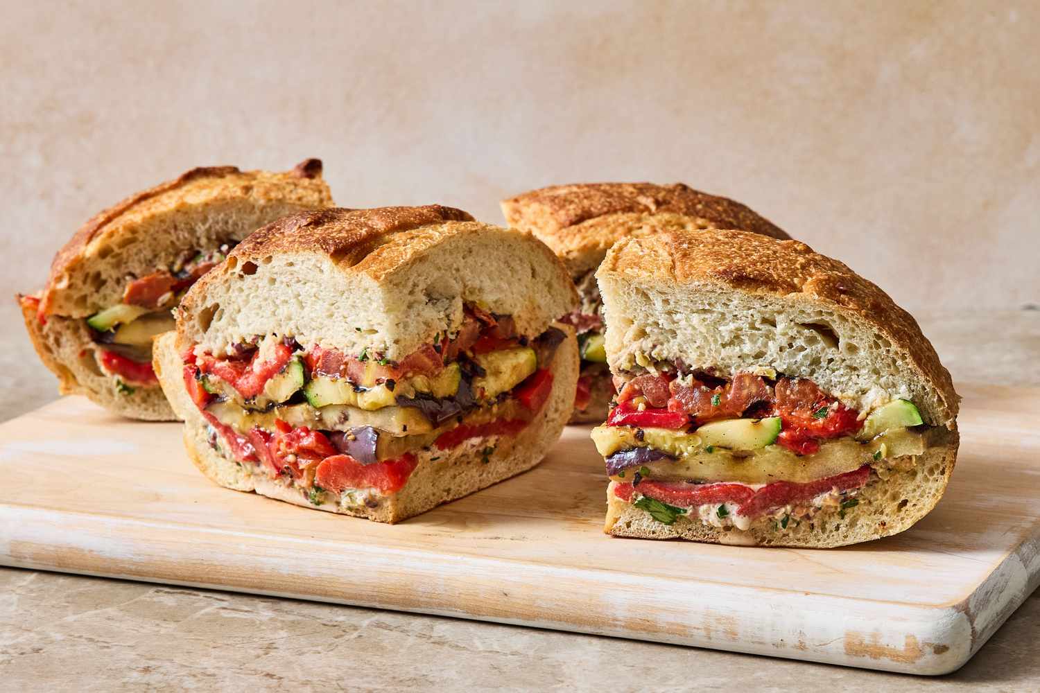 Slices of a grilled ratatouille muffuletta sandwich on a wooden board