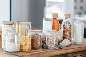 Various jars with grains legumes and food items displayed on a wooden surface